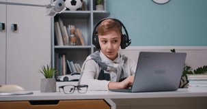 Boy wearing headphones, sitting at desk in his room and having online lesson on computer. Small kid in speak talk on video call, study distant. Online call.