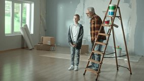 Grandpa and grandson are talking on video call using a mobile phone. A young guy is talking, waving hello and an older man is pushing a stepladder which then falls. Concept of repair in apartment.