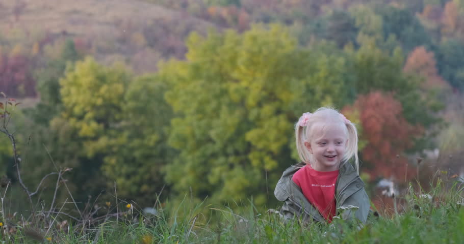 Little fair-haired girl sits in grass and plays with big apple. Child has fun in nature autumn day. Happy childhood