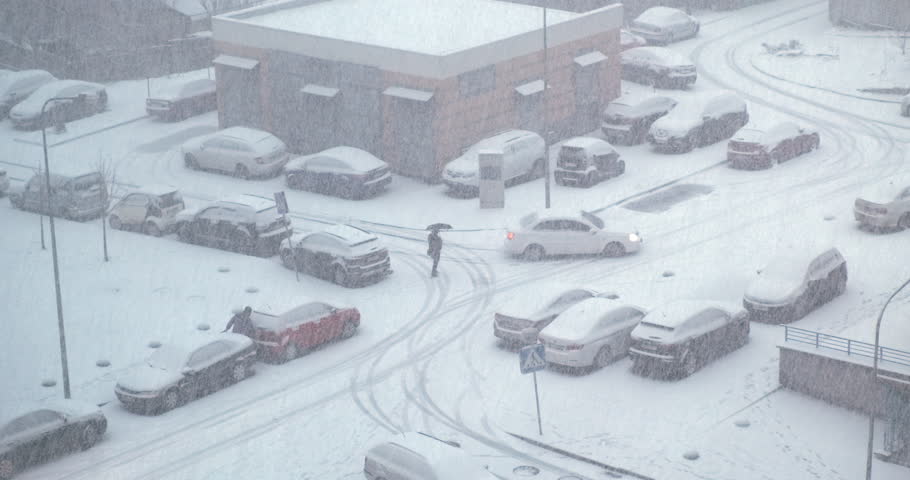 Top view, cars drive in heavy snow storm blizzard. Poor visibility, Europe city streets covered with white snow. Dangerous situation in snowy street. Winter snowfall cars covered in snow. Cold climate