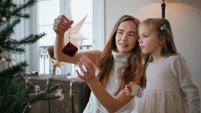 Adorable mom daughter decorating Christmas tree indoors closeup. Smiling woman giving xmas toy to baby at cozy room. Curious little girl putting decorations at green fir branch. New Year concept - Powered by Shutterstock - Get 15% off with code: PIKWIZARD15