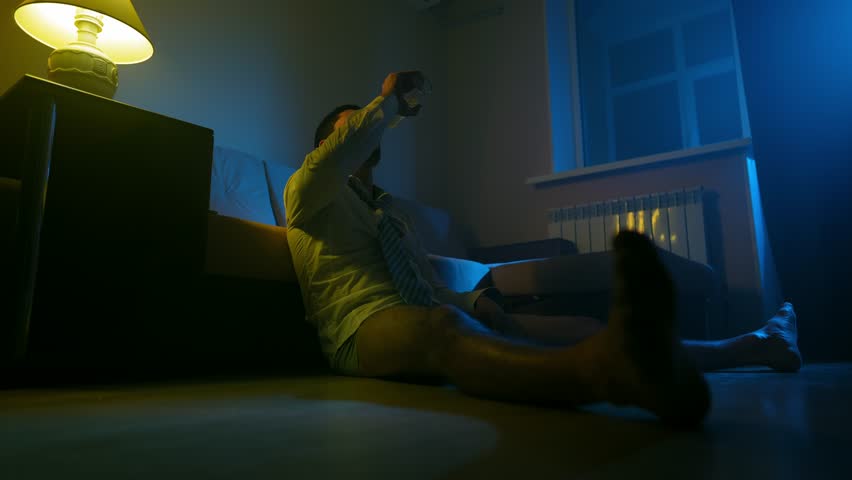 Depressed Business Man in an Office Shirt and Tie Without Pants Sits on Floor House and Drinks an Alcoholic Drink from a Glass Bottle in the Middle of the Night. Concept of Drunkenness and Alcoholism | Shutterstock HD Video #1099722757