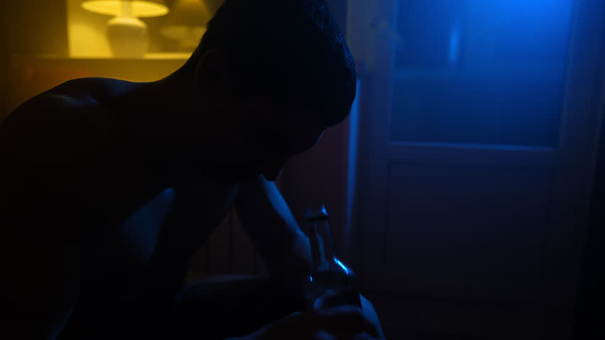 Silhouette of a Depressed Man Drinks Alcohol from a Glass Bottle at Night in the Dark. Problems with Alcoholism and Drug Addiction. Slow Motion. Royalty-Free Stock Footage #1099722767