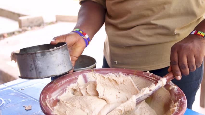 Person scooping mixed cake flour into cake pan for baking