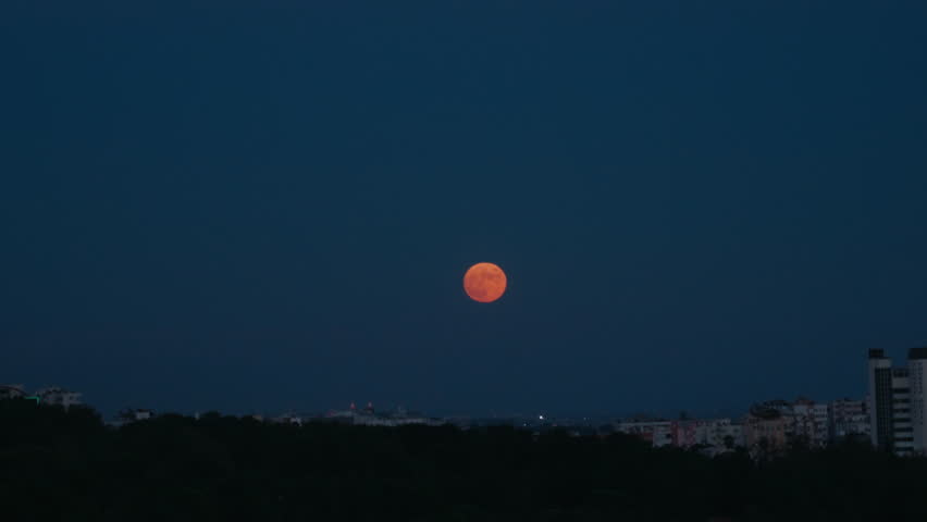 Red moon eclipse rising over city. Full moon in red or orange tint rising high over apartment buildings. 