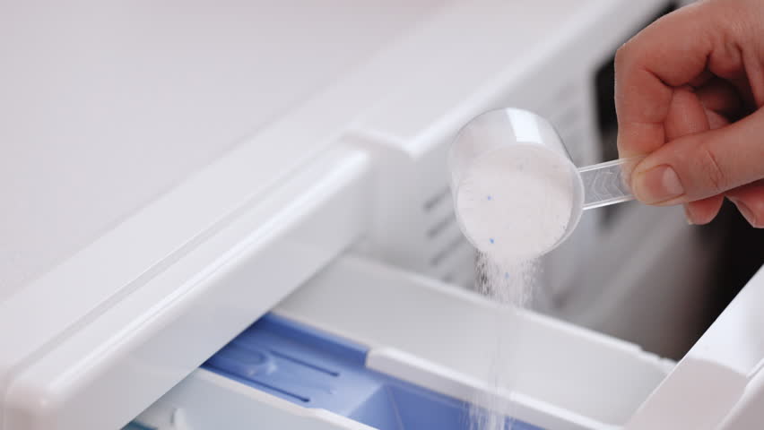 Woman carefully poured laundry detergent into compartment of washing machine in bathroom. With white measuring spoon person fills washing machine with powder. | Shutterstock HD Video #1099727739