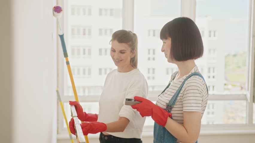 Two girls make repairs at home on their own. Close-up two women mark the wall under the water level. Girlfriends make repairs in the house. Woman measure wall with water level tool. | Shutterstock HD Video #1099728287