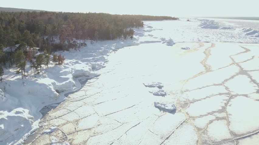 Northern Michigan icy shoreline of frozen Lake Superior. Drone shot of evening sunset, bright.