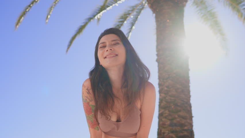 Close-up portrait of joyful young asian woman with dark hair and tattoo standing alone in seaside city smiling looking at camera. People and style concept. Palm trees ocean and mountains in background Royalty-Free Stock Footage #1099733177