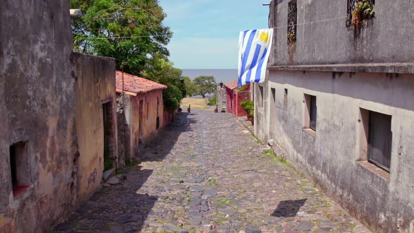 Panoramic view dolly in from the Calle de los suspiros in Colonia del Sacramento old town, Uruguay flag waving in slow motion. Sunny day Royalty-Free Stock Footage #1099734157