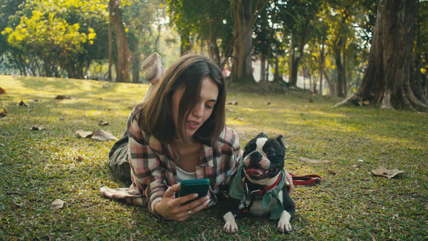 Young woman cuddles her Boston Terrier at sunset in the park