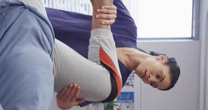 Vertical video of asian female doctor exercising with african american male patient at hospital. Medicine, healthcare, lifestyle and hospital concept.