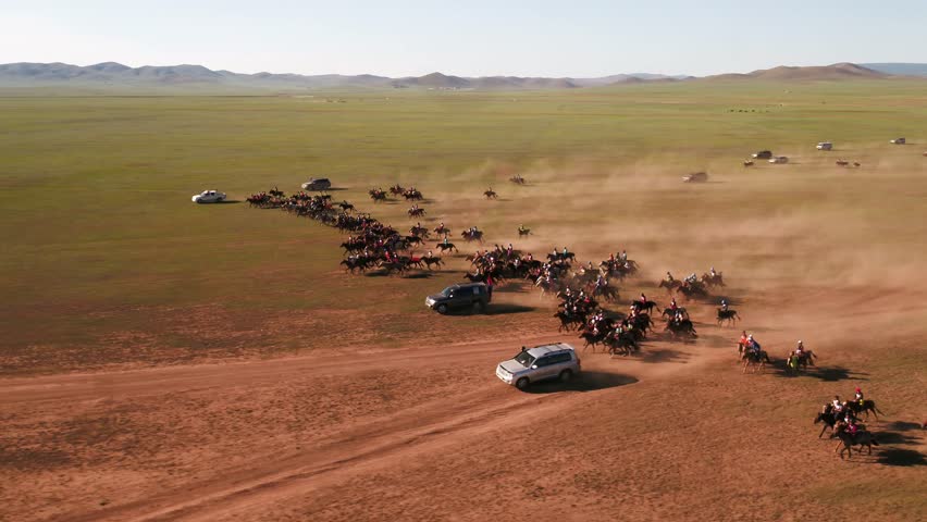 A group of Mongolian horseback riders training for a horserace in Mongolia called Naadaam. Dust covers the air as the horseback riders are followed by cars across the steppe. Royalty-Free Stock Footage #1099743109