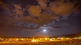 Time-lapse of sun disappearing into starry and cloudy sky over city of Morocco illuminated at evening