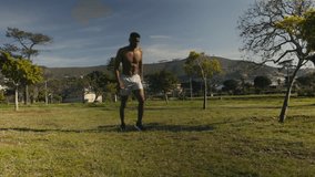 Topless young black man in shorts running during sports training drill in park
