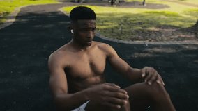Shirtless young black man wearing shorts doing sit-ups on pavement in park