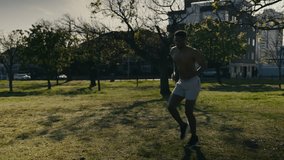 Shirtless young black man in shorts doing high knees cardiovascular exercise in park