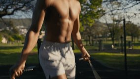 Topless young black man wearing shorts skipping with jump rope in park