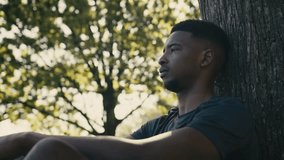 Young black man wearing t-shirt with eyes closed relaxing under tree in park