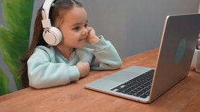 A little cute girl with white headphones watching a cartoon online on a laptop.