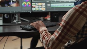 Young graphic designer artist editing video content on software, using focus lighting and color grading. Male filmmaker working on movie montage edit on pc multi monitors, cinematographer.