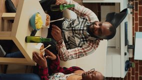 Vertical video: Happy life partners eating asian meal from delivery, serving noodles with chopsticks and watching comedy movie on tv. Modern couple in relationship enjoying show and food with alcohol.
