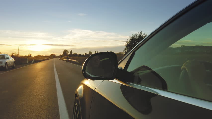 Driver view in the rear view of the sports car speeding on the road at sunset
