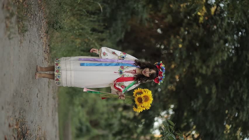 A beautiful Ukrainian woman in a Ukrainian national vyshyvanka dress with a bouquet of sunflowers runs towards the camera. war in Ukraine. War of Russia against Ukraine. vertical video