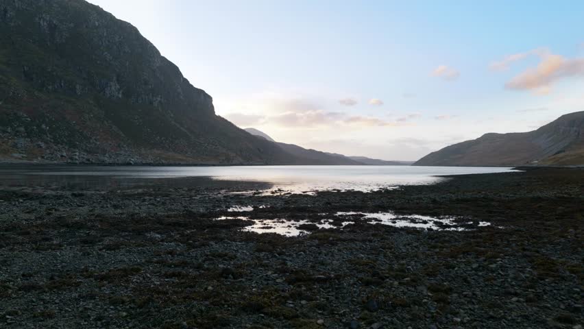 Ripples from the wind dance across the surface of a sea loch (Gleann Dubh) at low tide in the highlands of Scotland at sunset, surrounded by mountains.