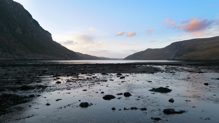 Water slowly flows into a sea loch (Gleann Dubh) at low tide in the highlands of Scotland at sunset, surrounded by mountains.