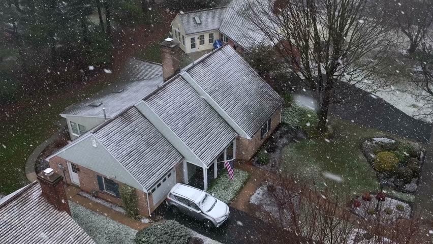 Aerial top down establishing shot of American home during winter snowstorm. American flag waving outside during blizzard.
