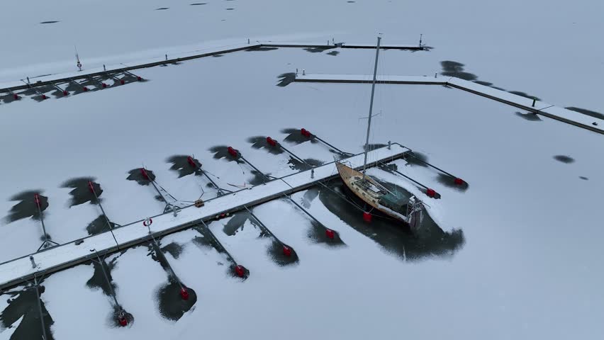 Aerial View of dead frozen harbour docks with boat and ice below. Extreme cold weather. Nature landscape famous for being heavily affected by global warming and Climate Change. Mooring for yachts