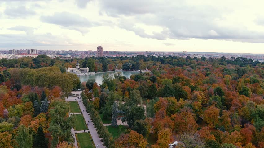 The drone is flying over Parque del Buen Retiro towards Monumento Alfonso XII with automn color trees and the city in the background in Madrid Spain Aerial Drone Footage 4k