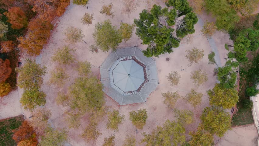 The drone is flying up looking topdown at Retiro Park Bandstand in Parqe del Buen Retiro with autumn color trees around in Madrid Spain Aerial Drone Footage 4K