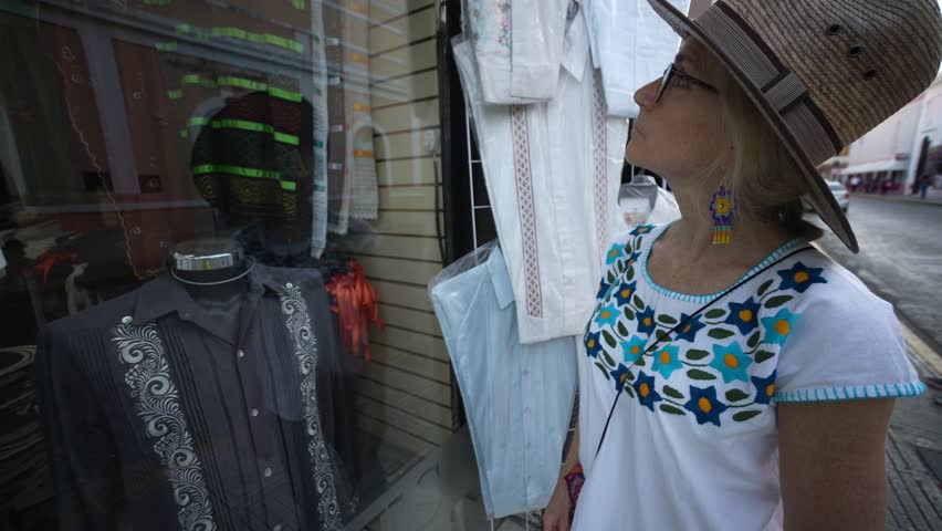 Closeup of pretty mature senior woman tourist wearing ethnic clothes looking in window of tourist souvenir shop in Merida, Yucatan, Mexico.