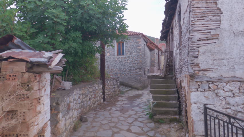 Day POV walking to an empty cobblestone alley around old low-rise stone-built houses with red tiles at Prespes lake area, Greece.