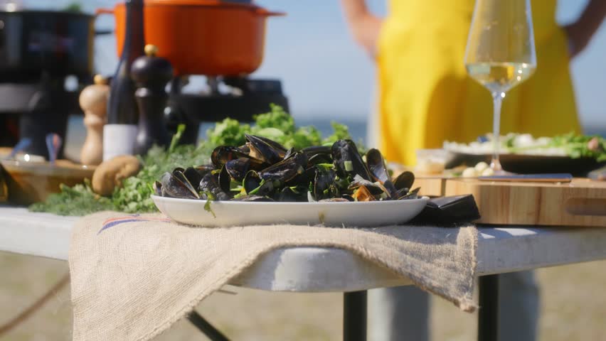 A table with a plate full of mussels and a hand grabbing one mussel to open and eat in slowmotion