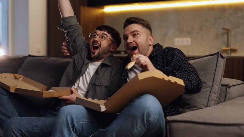Two friends are sitting on the couch and eating pizza. | Shutterstock HD Video #1099775137