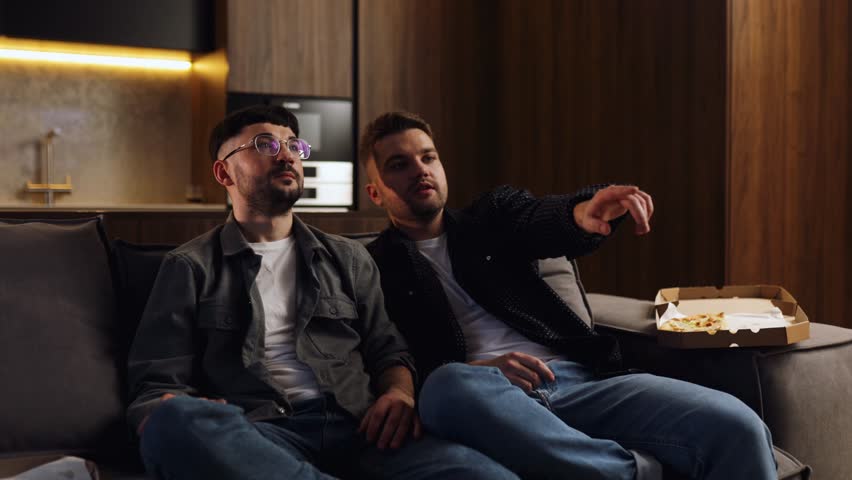 Friends looking disappointed about final score. Two bearded man spending weekend together at home, sitting on sofa, watching soccer play live broadcast on tv | Shutterstock HD Video #1099775141
