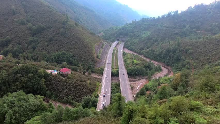Aerial view of road bridges and highway tunnels in forested mountain valley.
