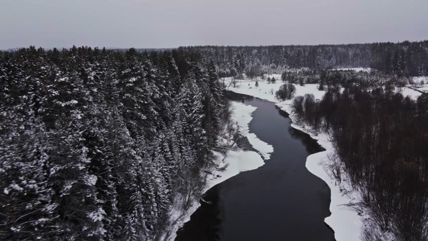 Frozen winter river with ice through snow-covered forest landscape