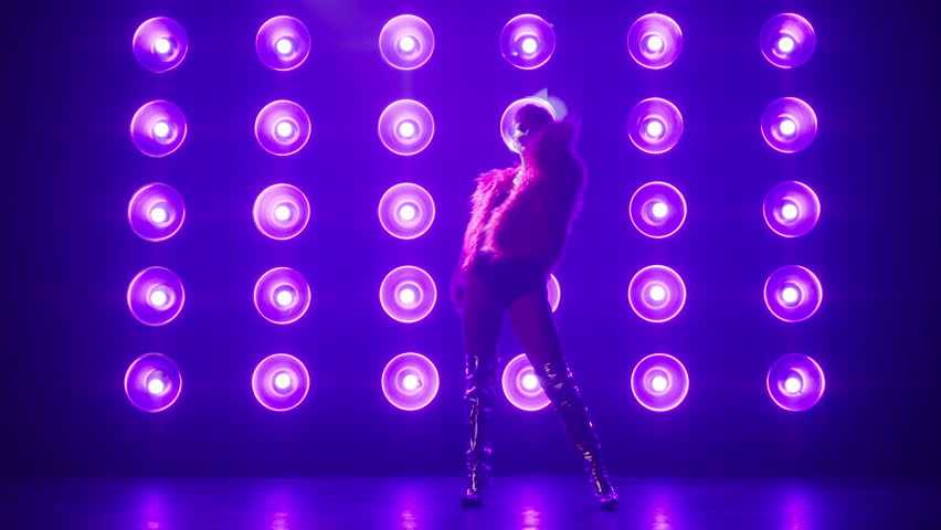 Slim fit active woman dancing RnB style moves, spinning on floor, performing choreography for show on stage. Female silhouette in stylish show outfit costume fluffy pink fur coat, shiny silver boots 