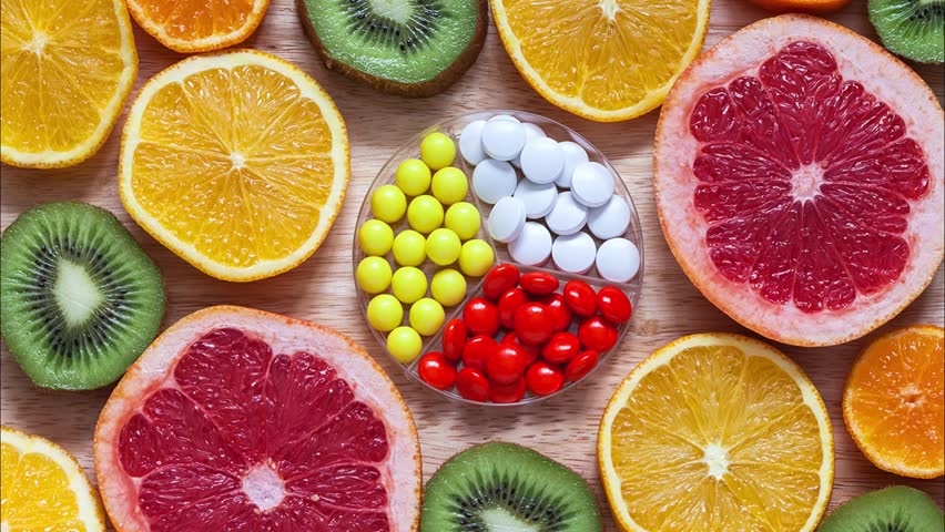 Bright background of fresh sliced healthy fruits and set of vitamins in form of tablets in center. Concept of taking care of health, boosting immunity, taking vitamin preparations. Flat lay, close-up Royalty-Free Stock Footage #1099782453