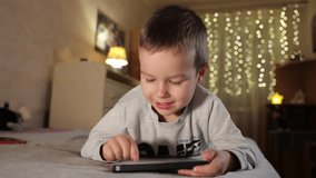 Cute Little Boy Uses Phone At Home in Room. Kid Plays Mobile Games On Smartphone Smiling and Showing Emotions