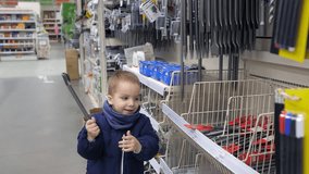Slow motion video of the 3 years old caucasian boy playing with a building tool in hardware store. Preparation for repair. Side view of cute kid in construction equipment department of day shop. 