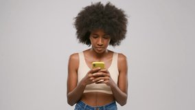 Afro american girl is reading message looking at smartphone on grey background.