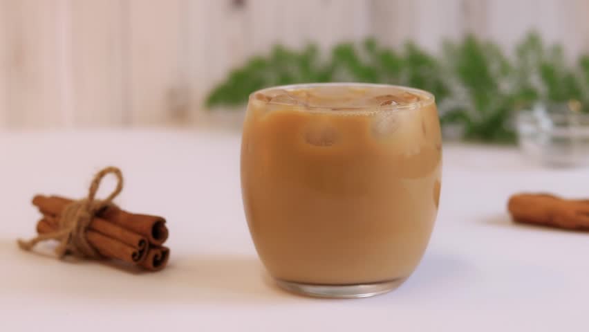Iced coffee with milk, a refreshing invigorating drink. Stir the finished coffee with milk with a straw, mix | Shutterstock HD Video #1099793581