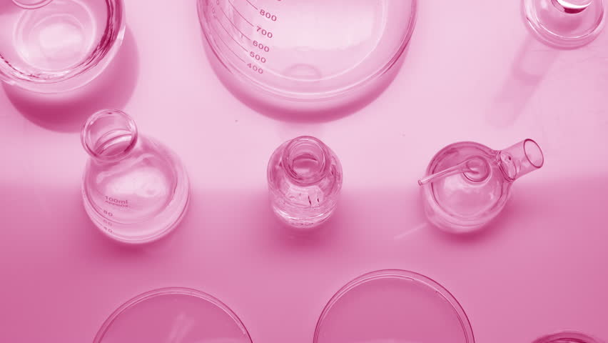 Close-up crane shot of water drops drip into reagent bottle surrounded by lab glassware with water on pale pink background | Background shot for skin moisturizing cosmetics commercial Royalty-Free Stock Footage #1099794515