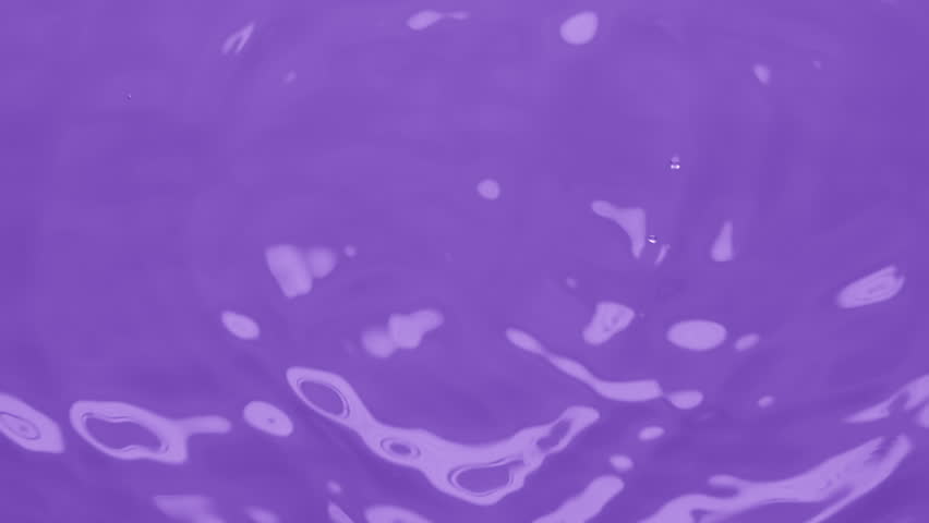 Macro crane shot of water drops fall down on water surface creating water rings on violet background | Skin moisturizing concept
