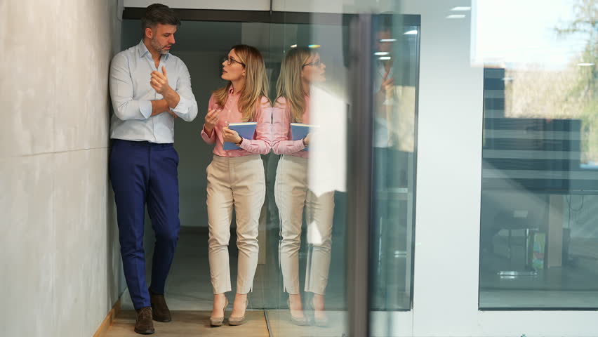 Cheerful businessman and business female manager with glasses and notebook in her hands walking through office hallway in modern corporate building, talking, having fun conversation, laughing, bonding | Shutterstock HD Video #1099795995